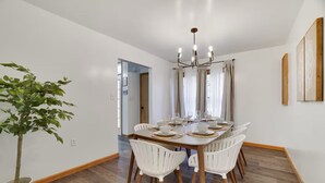 A dining area with a wooden table set for six, white chairs, a chandelier, and a potted plant. - Modern 3BR,Game Room , FirePit& 15 mins away from Ski Resort (East Stroudsburg)