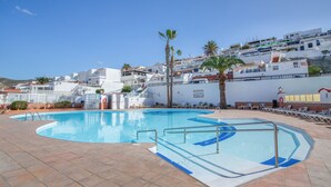 Une piscine entourée d’une terrasse carrelée, de palmiers et bordée d’immeubles blancs.