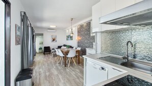 Une cuisine moderne avec des meubles blancs, un évier en acier inoxydable et un coin repas comprenant une table et des chaises en bois.