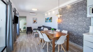 Une cuisine moderne avec un coin repas, un mur recouvert d’un tableau noir où sont écrits des mots, et un téléviseur à écran plat.
