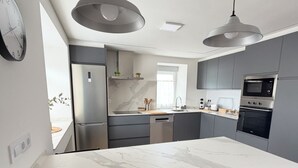 A modern kitchen with a marble island, black chairs, a built-in oven, and pendant lighting. - La Quintana de Pola (Brand-new luxury country retreat in Cudillero) (Cudillero)