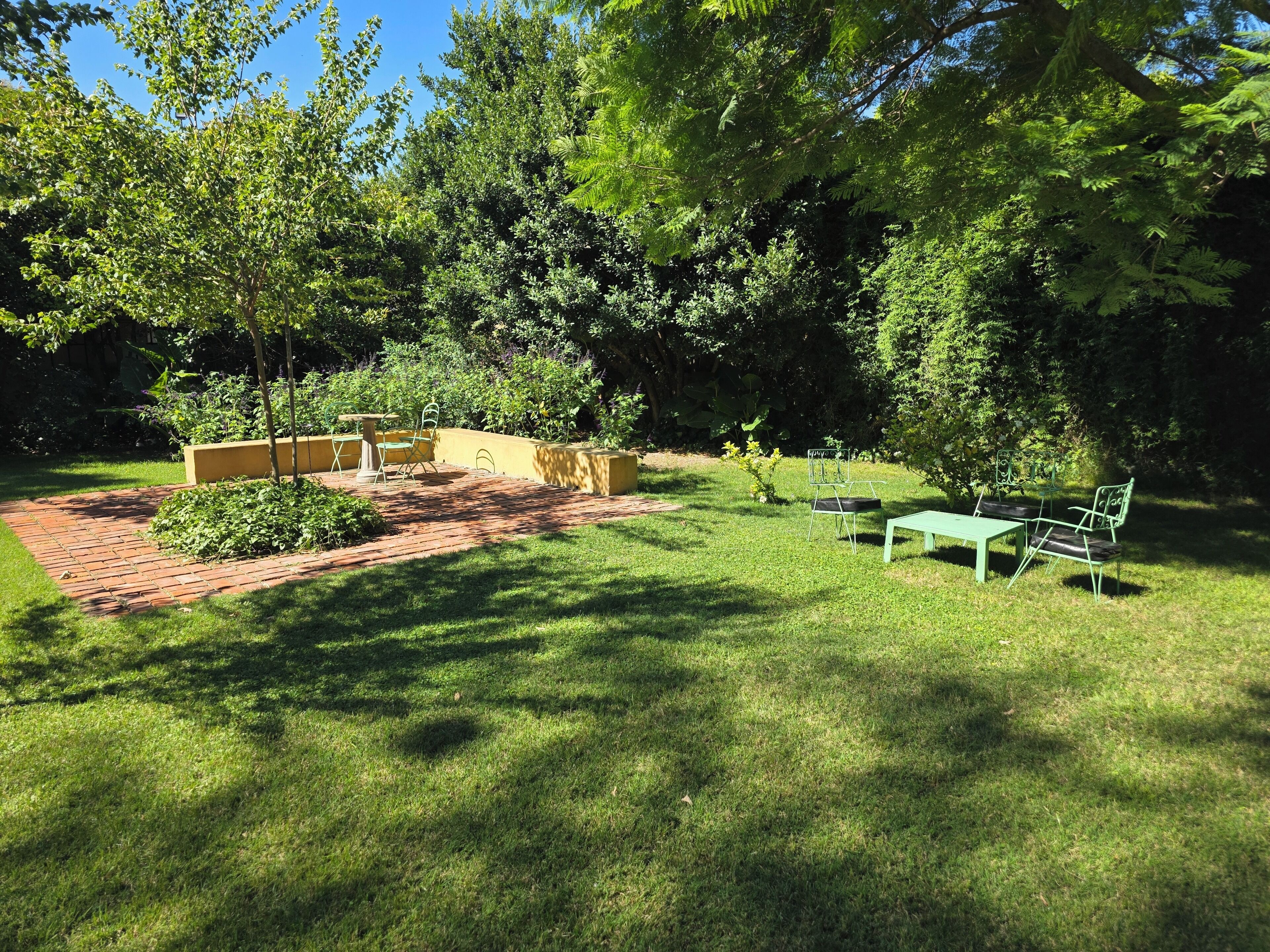 A patio area with a brick pathway, green lawn, and outdoor furniture including a table and chairs.