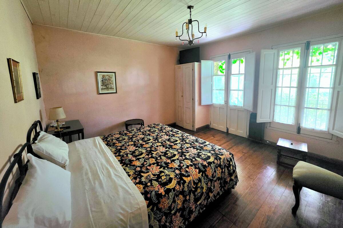Ein Schlafzimmer mit Bett, Schreibtisch, Stuhl, einer Chandelierleuchtre und einem Fenster mit Rollläden.