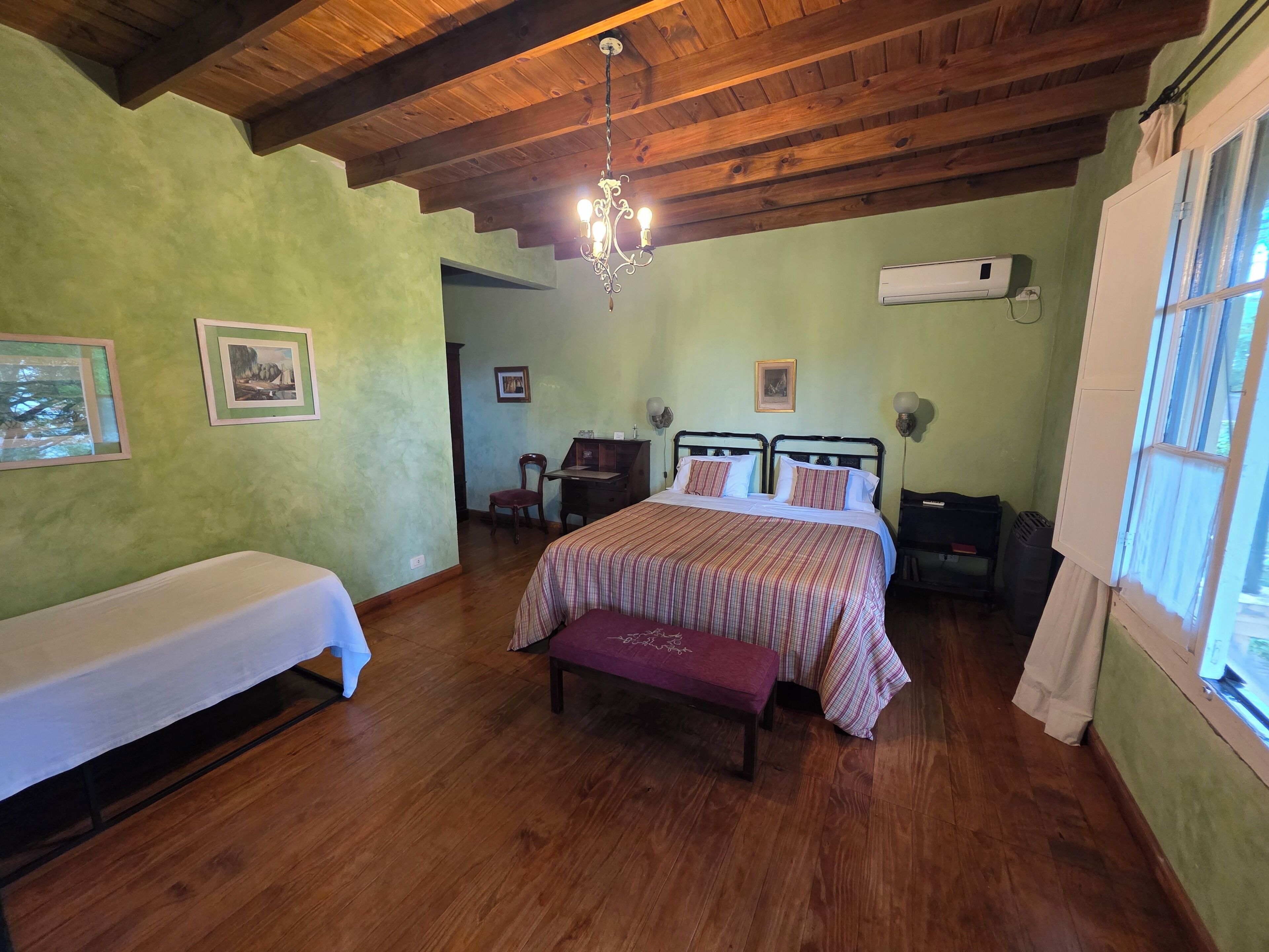 Een slaapkamer met een houten plafond, een bed met een gestreept beddegoed, een bankje, een stoel en een bureau.