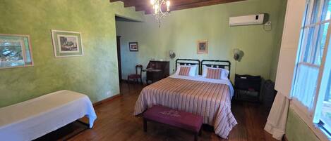 A bedroom with a wooden ceiling, a bed with a striped bedspread, a bench, a chair, and a desk.