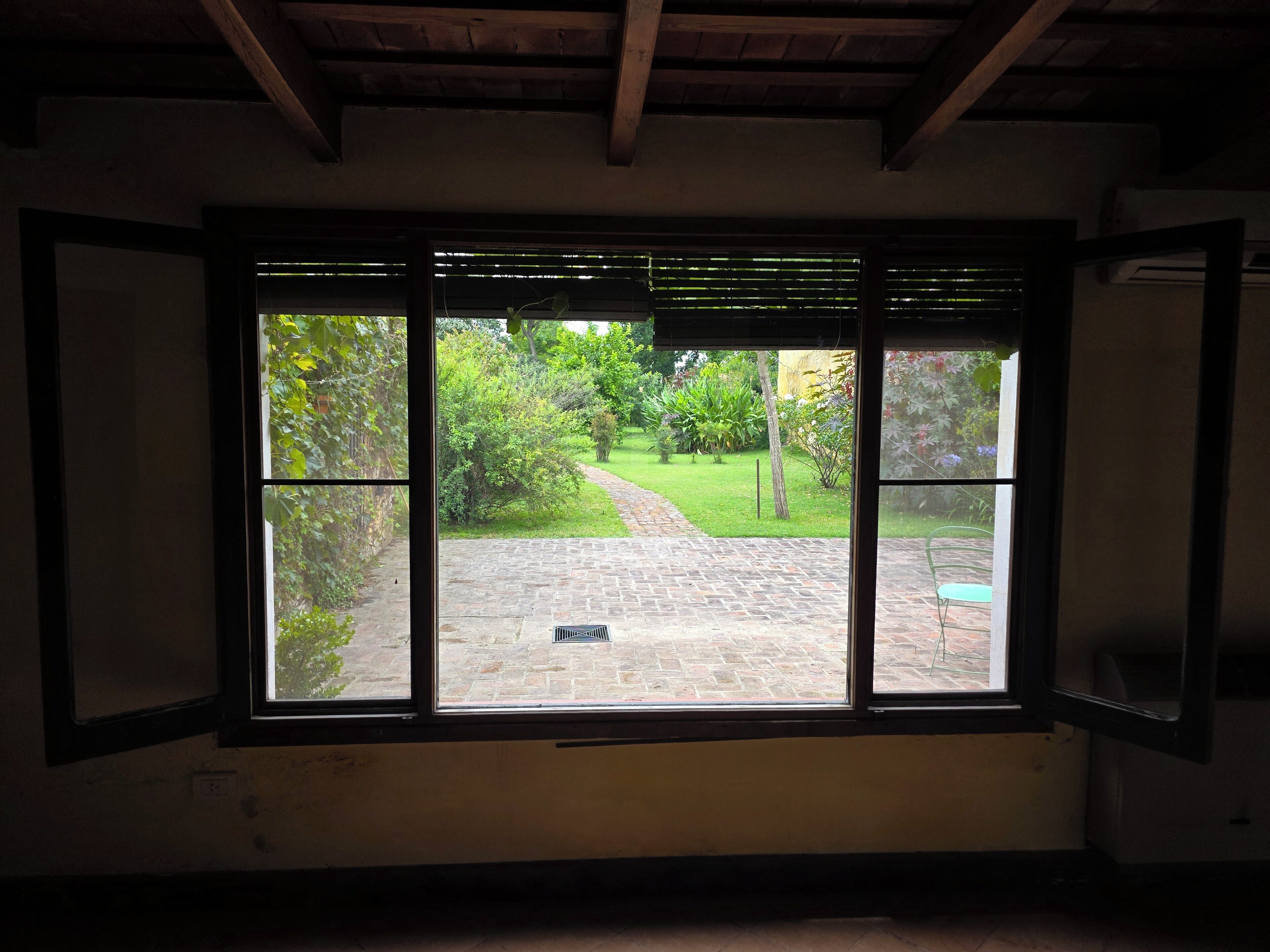 Ein Zimmer mit großem Fenster und Blick auf einen Garten mit einem Pflasterweg.