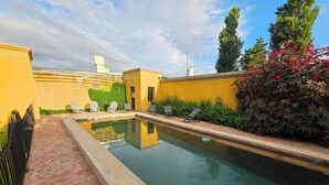 Une piscine dotée d’une terrasse carrelée, entourée de murs jaunes et de verdure.
