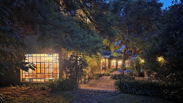 Un chemin de jardin qui mène à un bâtiment doté de grandes fenêtres et d’une entrée en briques.