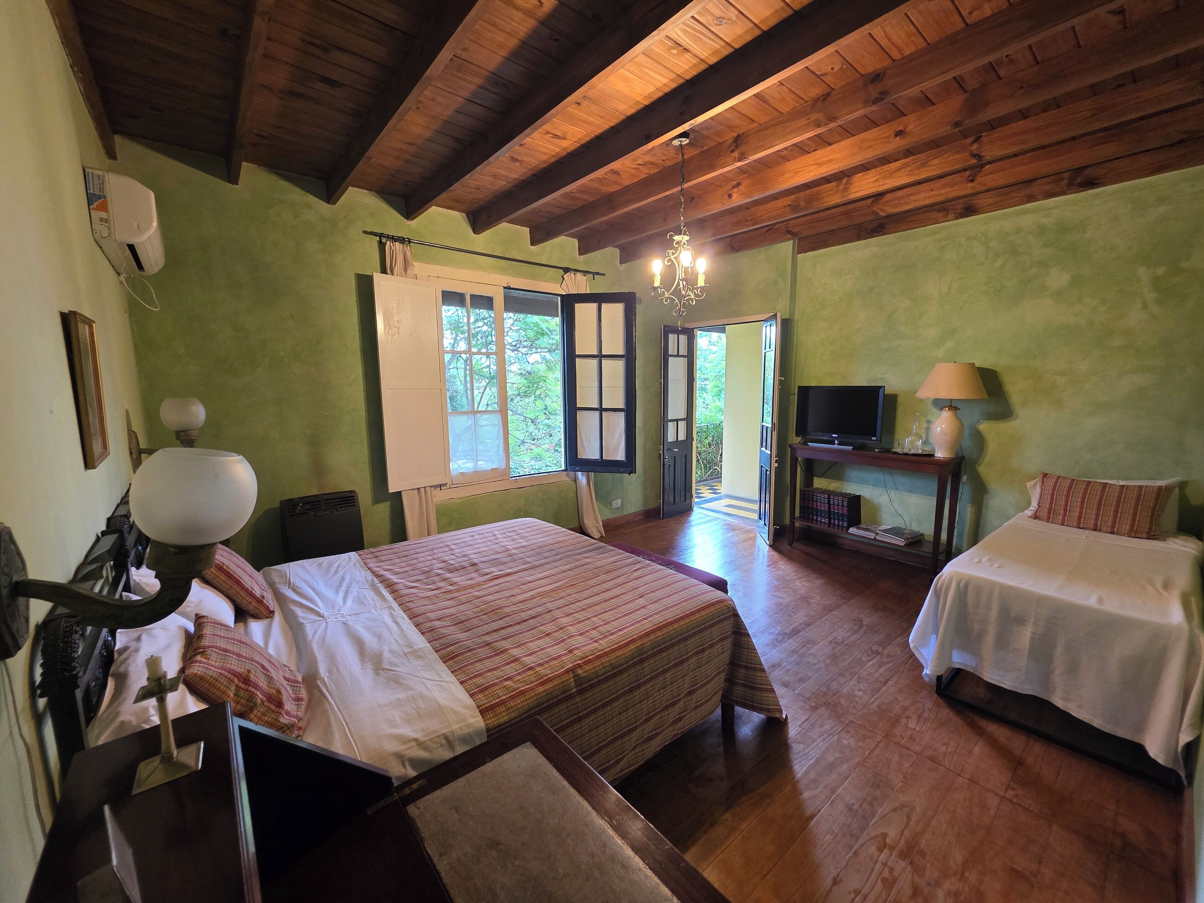 A room with two beds, a television, a lamp, and a window with curtains.