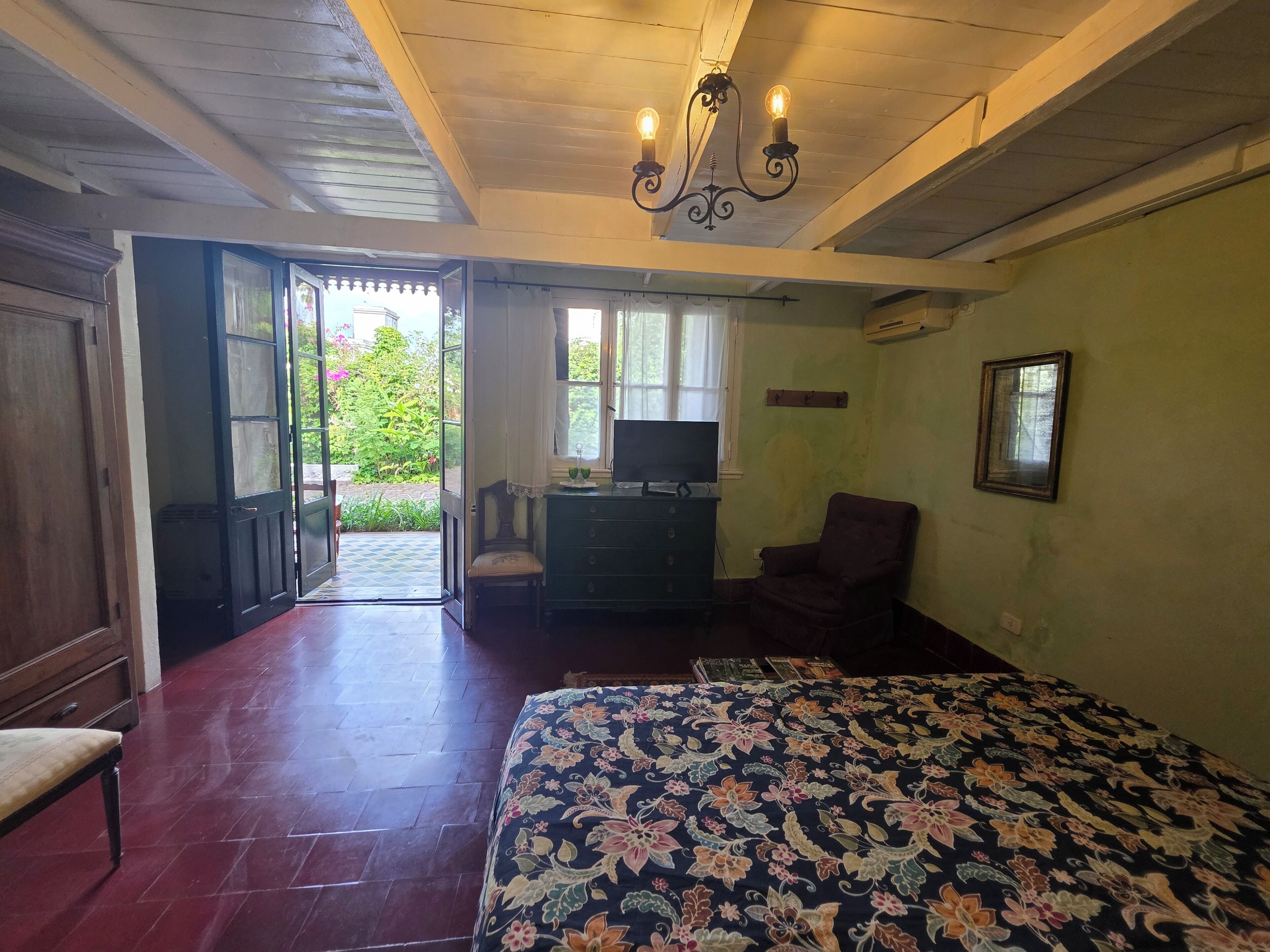 A bedroom with a bed, a desk with a chair, a television, and a window.