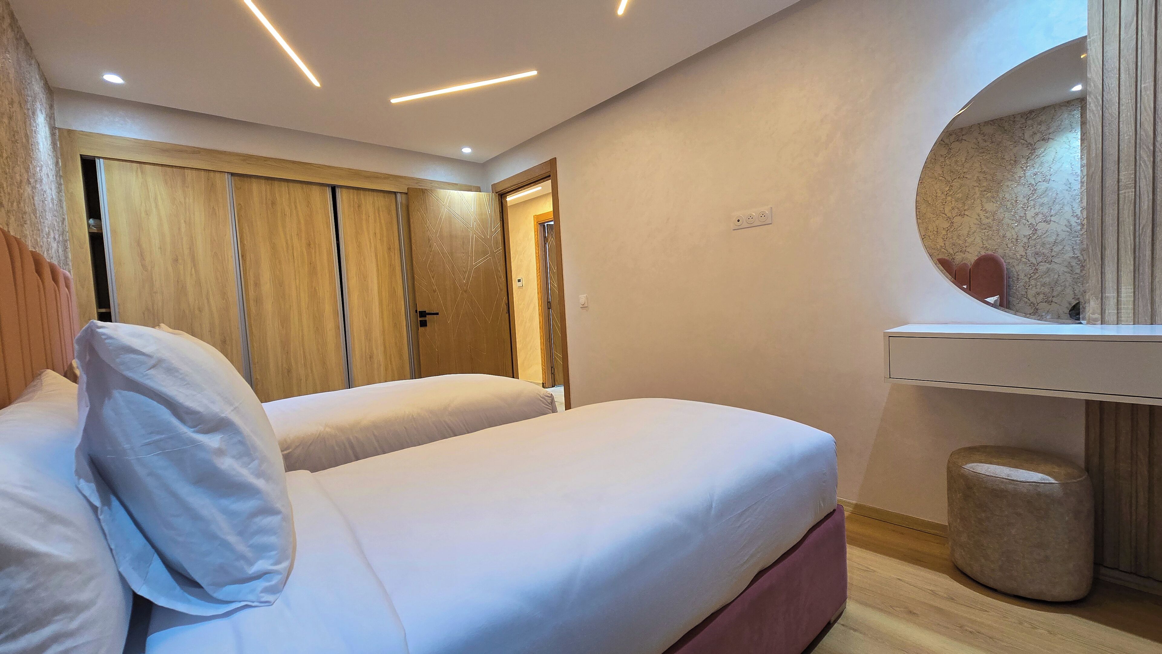 Habitación de hotel con dos camas, un armario de madera, un espejo y un pequeño espejo redondo sobre un aparador.