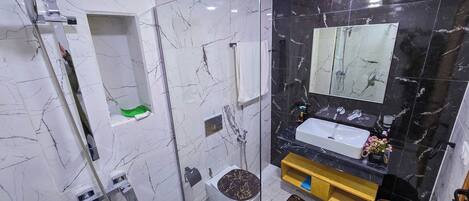 A modern bathroom with a glass-enclosed shower, a white toilet, a sink with a mirror above, and a marble-tiled wall.