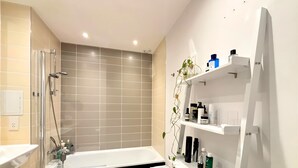 A modern bathroom with a bathtub, a shower, and a shelf with toiletries. - The Designer Skyline (Greater London)