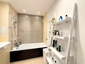 Une salle de bain moderne équipée d’une baignoire, d’une douche et d’une étagère pour les articles de toilette.