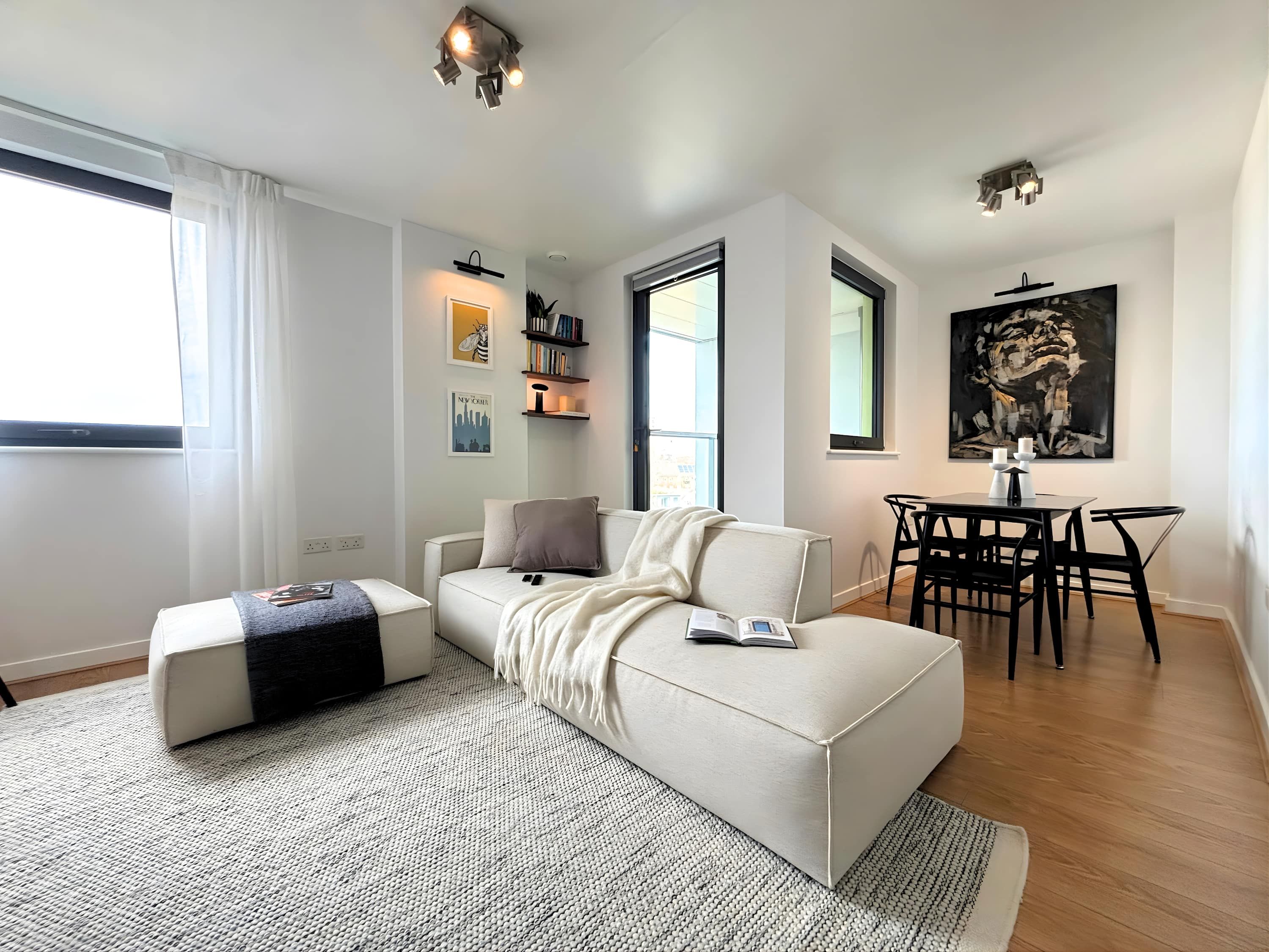 Uma sala de estar moderna com um sofá, uma mesa de centro, uma área de refeições com mesa e cadeiras, e um grande quadro abstrato na parede.