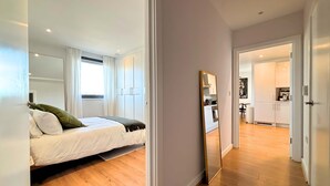 A modern bedroom with a bed, a large mirror, and a view into the kitchen. - The Designer Skyline (Greater London)