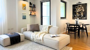 A modern living room with a sofa, a dining table with chairs, a bookshelf, and a large abstract painting. - The Designer Skyline (Greater London)
