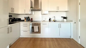 A modern kitchen with white cabinetry, a stainless steel range, and an oven. - The Designer Skyline (Greater London)