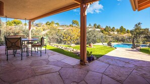 A covered patio with a stone floor, outdoor furniture, and a view of a backyard with a swimming pool and a lawn. - Pool Days, Play Days, Paws Welcome (Cottonwood)