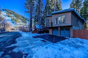 A two-story house with a garage, surrounded by snow-covered ground and trees. - Luxury Slopeside Ski Haus | Hot Tub + Sauna | 12P (South Lake Tahoe)