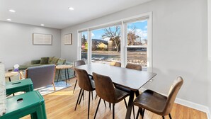 A dining area with a large table and chairs, a sofa, and a view of the outdoors.