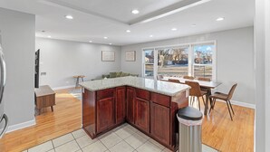 A modern kitchen with a wooden island, a dining area with chairs, and a large window offering a view of the outside.