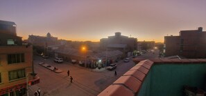 Une vue de rue au crépuscule, avec des bâtiments, des véhicules et quelques piétons.