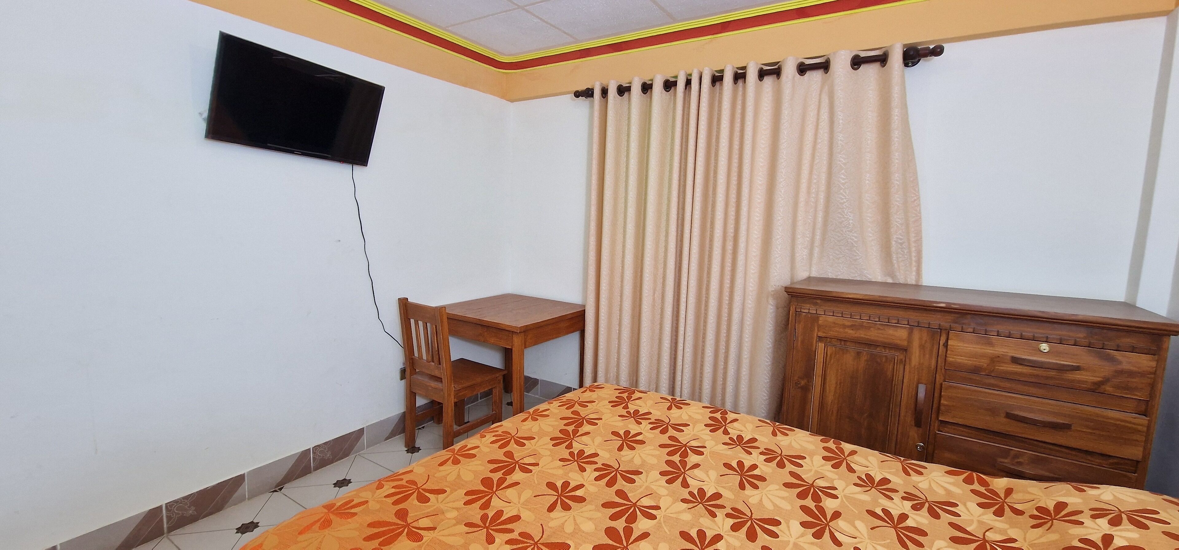 Un dormitorio con cama, escritorio de madera, silla, armario y televisor montado en la pared.