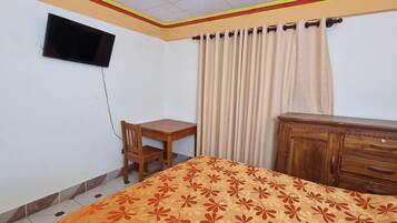 Un dormitorio con cama, escritorio de madera, silla, armario y televisor montado en la pared.