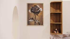 Un tableau encadré représentant une rose, accroché au mur, une étagère en bois avec un vase de fleurs et un sol carrelé.