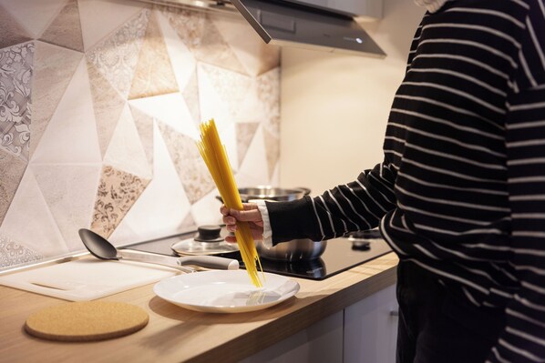 Eine Küchenarbeitsplatte mit einem Teller, einem Korkuntersetzer und einer Person, die Spaghetti hält.