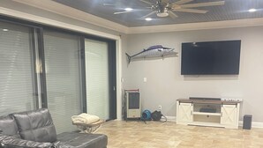 Ein modernes Wohnzimmer mit Ledersofa, Deckenventilator, Wand-Fernseher und einer Fischdekoration an der Wand.