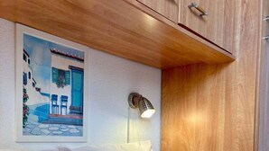 A neatly made bed with white linens and a beige pillow, a wall-mounted lamp, and a framed painting of a blue building. - Casa Romana, the Southern Style Cottage (Balaruc-les-Bains)