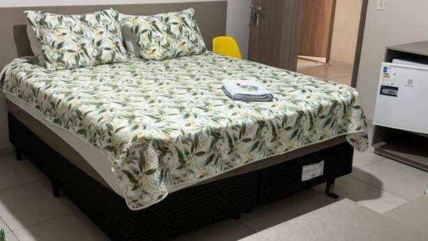 A bed with floral bedding, a bedside table, a chair, a door, and a wall-mounted artwork. - Hotel Master Plaza Formiga (Formiga)