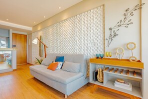A modern living room with a sofa, a coffee table, and a wall-mounted shelf with decorative items. - BR19 Beautiful Apartment 300m from Barra Beach (Salvador)