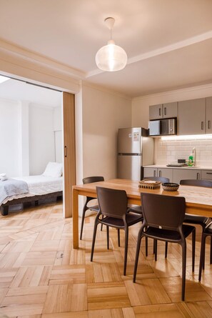 A modern kitchen with a refrigerator, microwave, and wooden dining table with chairs. - Luxury 1BR Loft in Bellavista | Near Metro Fits 5 (Providencia)