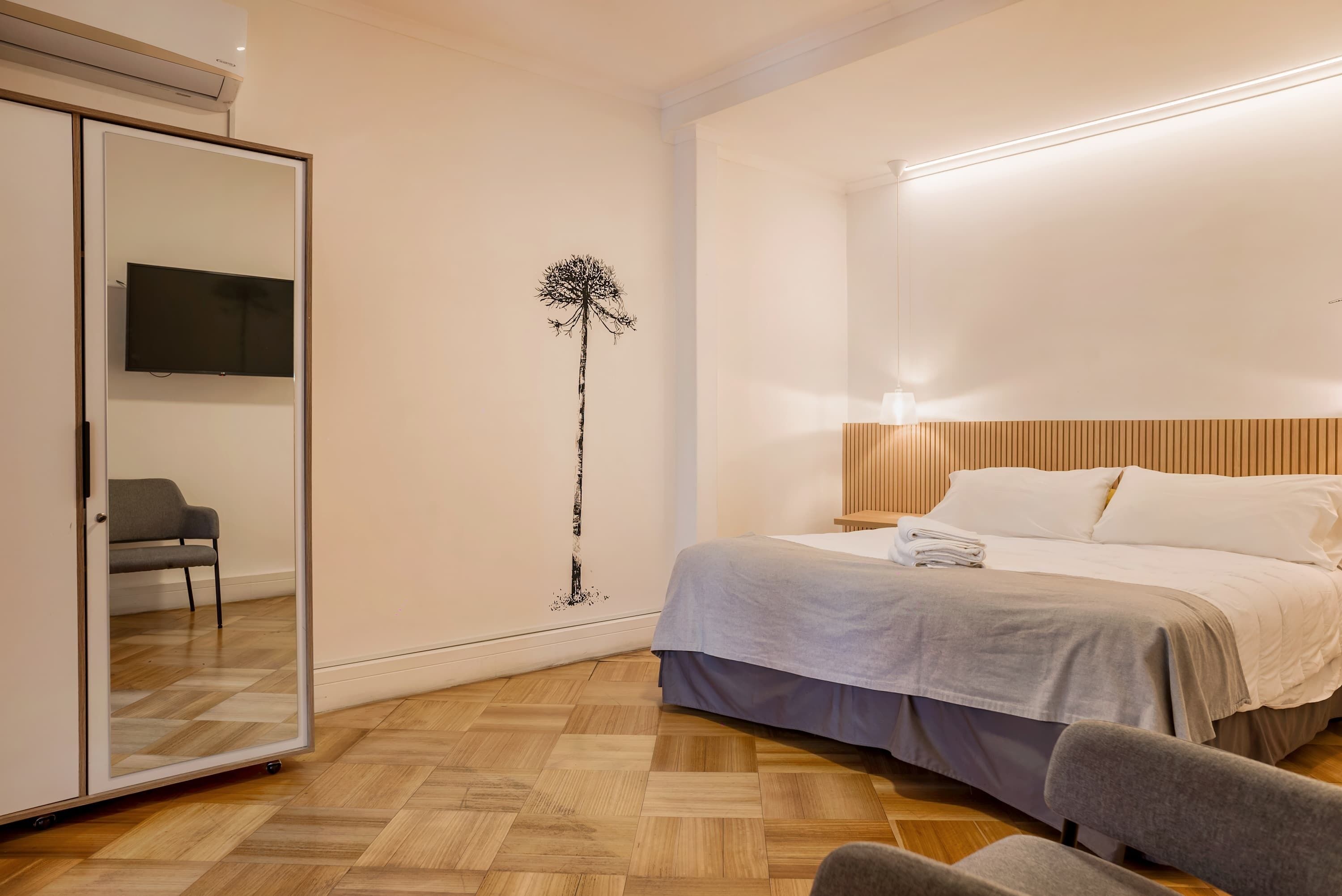 A bedroom with a bed, a mirror, a TV, a chair, and a wall art piece.
