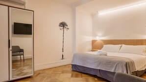 A bedroom with a bed, a mirror, a TV, a chair, and a wall art piece. - Luxury 1BR Loft in Bellavista | Near Metro Fits 5 (Providencia)