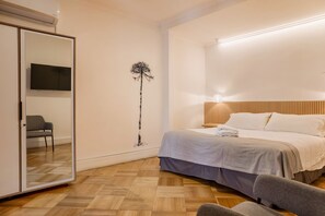 A bedroom with a bed, a mirror, a TV, a chair, and a wall art piece. - Luxury 1BR Loft in Bellavista | Near Metro Fits 5 (Providencia)
