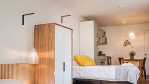 A hotel room with two beds, a wooden wardrobe, a desk with a chair, and a hanging light fixture. - Cozy Studio Bellavista Dining & Hospital Access (Providencia)