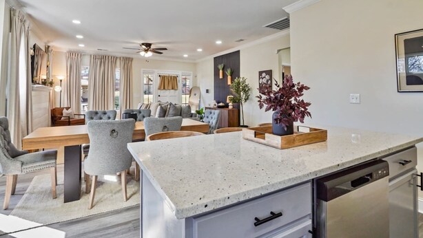 A modern kitchen with a central island, dining area with grey upholstered chairs, and a ceiling fan. - Beautifully Renovated Historic 4 BR Home|Sleeps 16 (Birmingham)