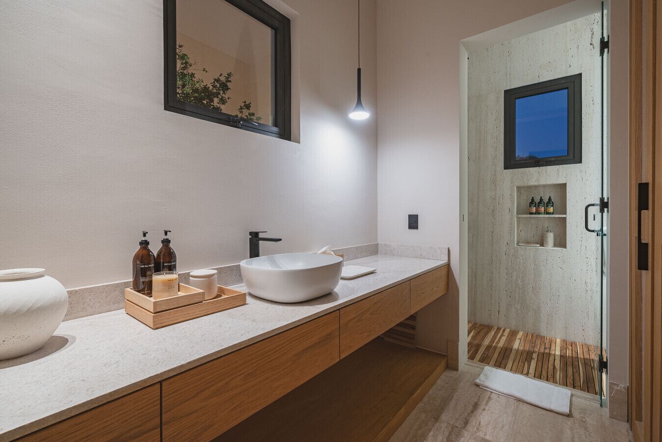 A modern bathroom with a large white sink, wooden cabinets, and a glass shower enclosure.