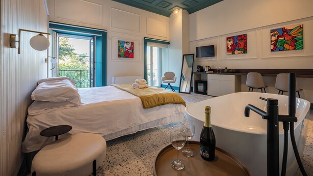 Une chambre d’hôtel comprenant un lit, un coin salon, une baignoire et des œuvres d’art accrochées aux murs.