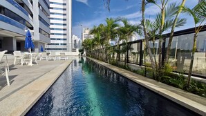 A modern hotel pool area with lounge chairs and umbrellas, surrounded by palm trees and a clear sky. - COCAR0115 - Salvador Prime (Salvador)