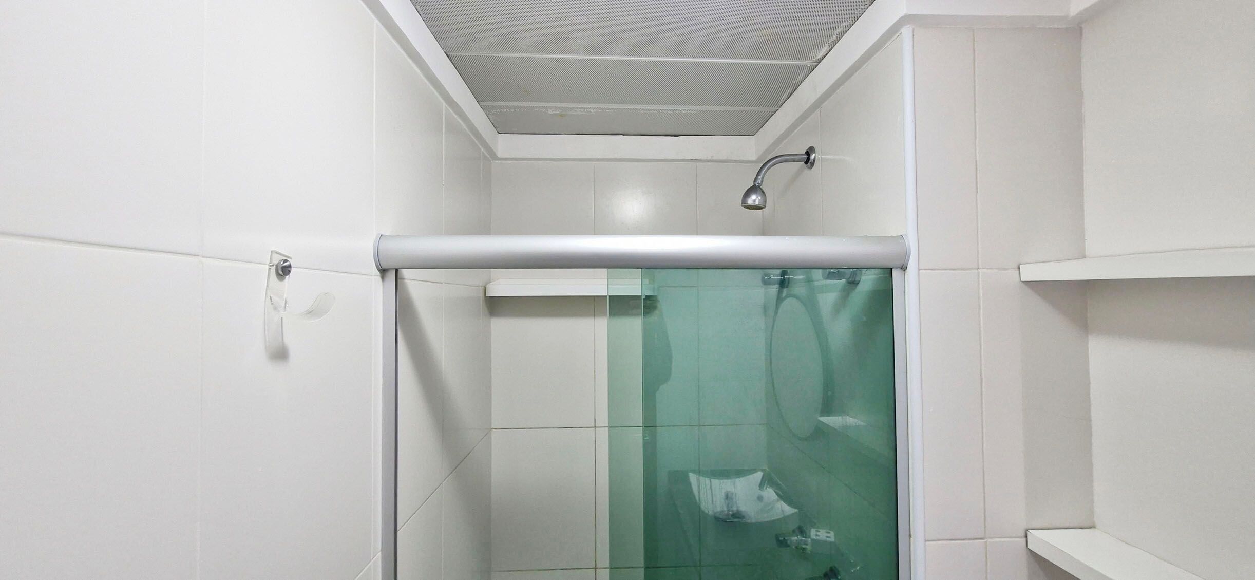 A bathroom with white walls, a glass shower enclosure, and a ceiling vent.