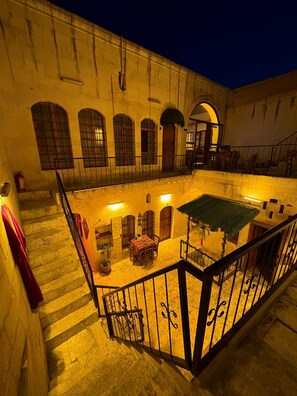 A courtyard with a dining area, a staircase, and a building facade with arched windows and doors. - Ayataç Konak Otel (Sanliurfa)