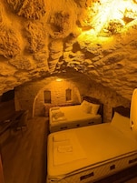 Una habitación con pared de piedra, cama, escritorio y una ventana pequeña.