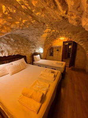 Een kamer met een stenen plafond, een bed met witte lakens, een houten hoofdeinde en een klein houten kastje.