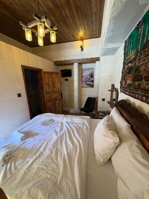 A bedroom with a large bed, a wooden wardrobe, a chair, and a wall-mounted TV. - Ayataç Konak Otel (Sanliurfa)