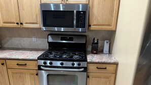 Uma cozinha com armários de madeira, micro-ondas de aço inoxidável, fogão a gás e forno.